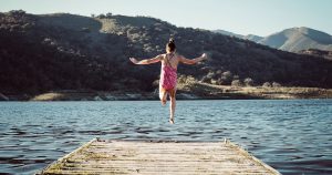 Girl jumping off a dock into a lake.